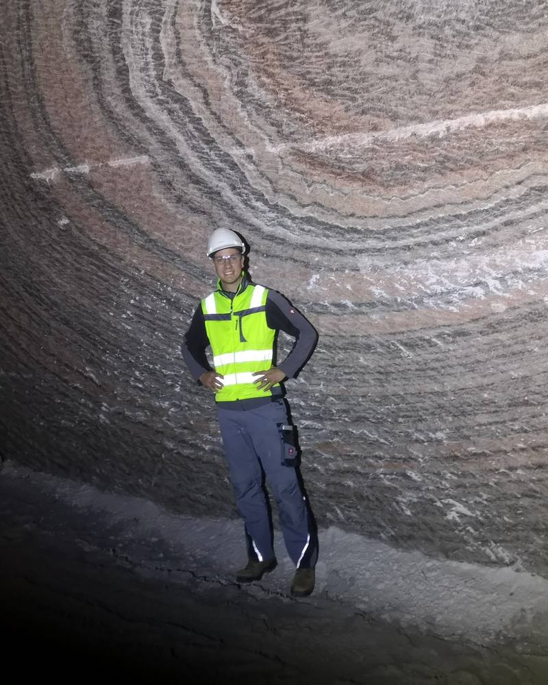 Carlo Borns mit Schutzhelm, Schutzbrille und Warnweste unter Tage vor einer gebänderten Salzwand in einem Salzbergwerk